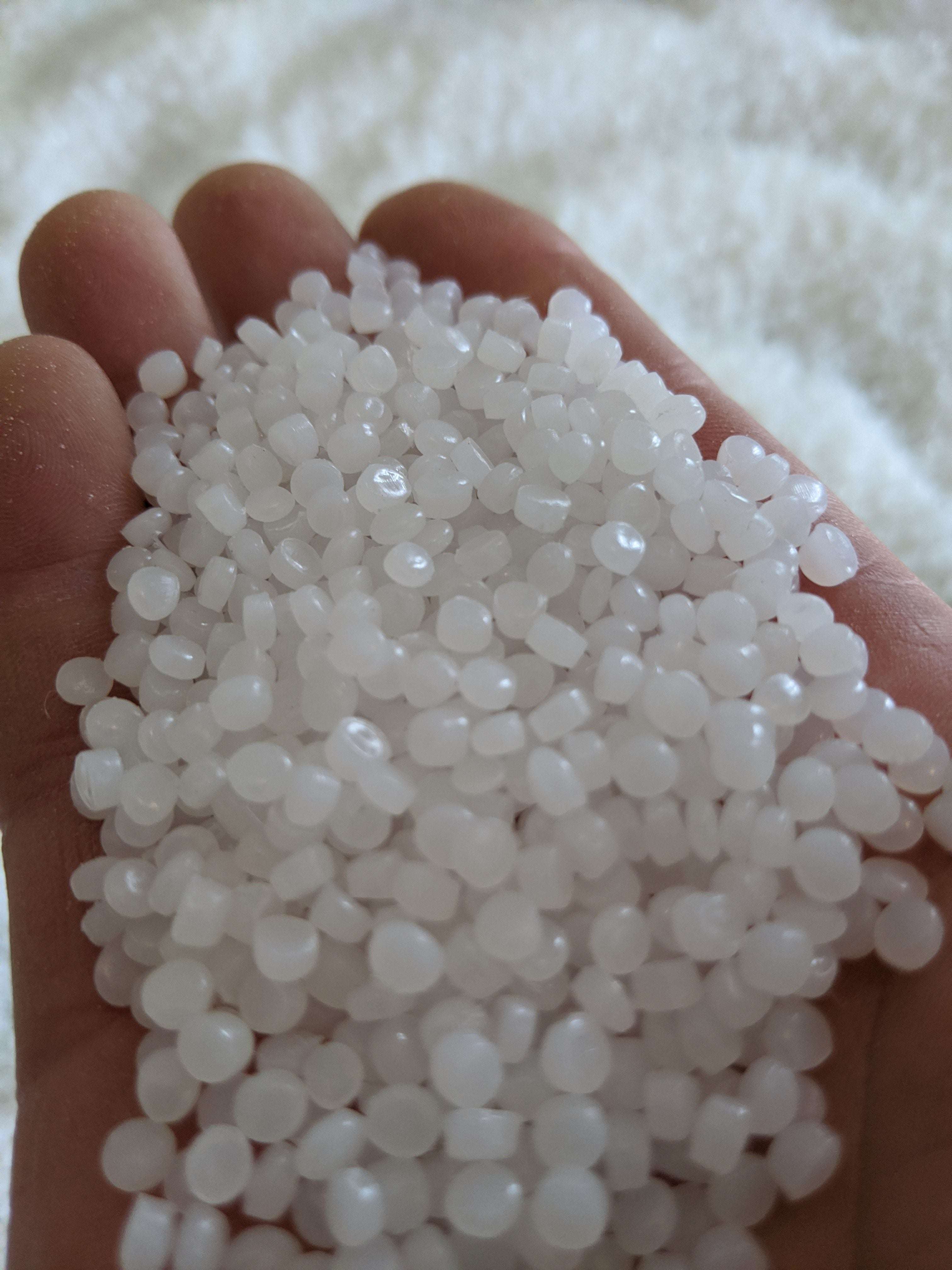 Handful of small, milky white translucent sensory beads with a smooth, round shape held in a palm.