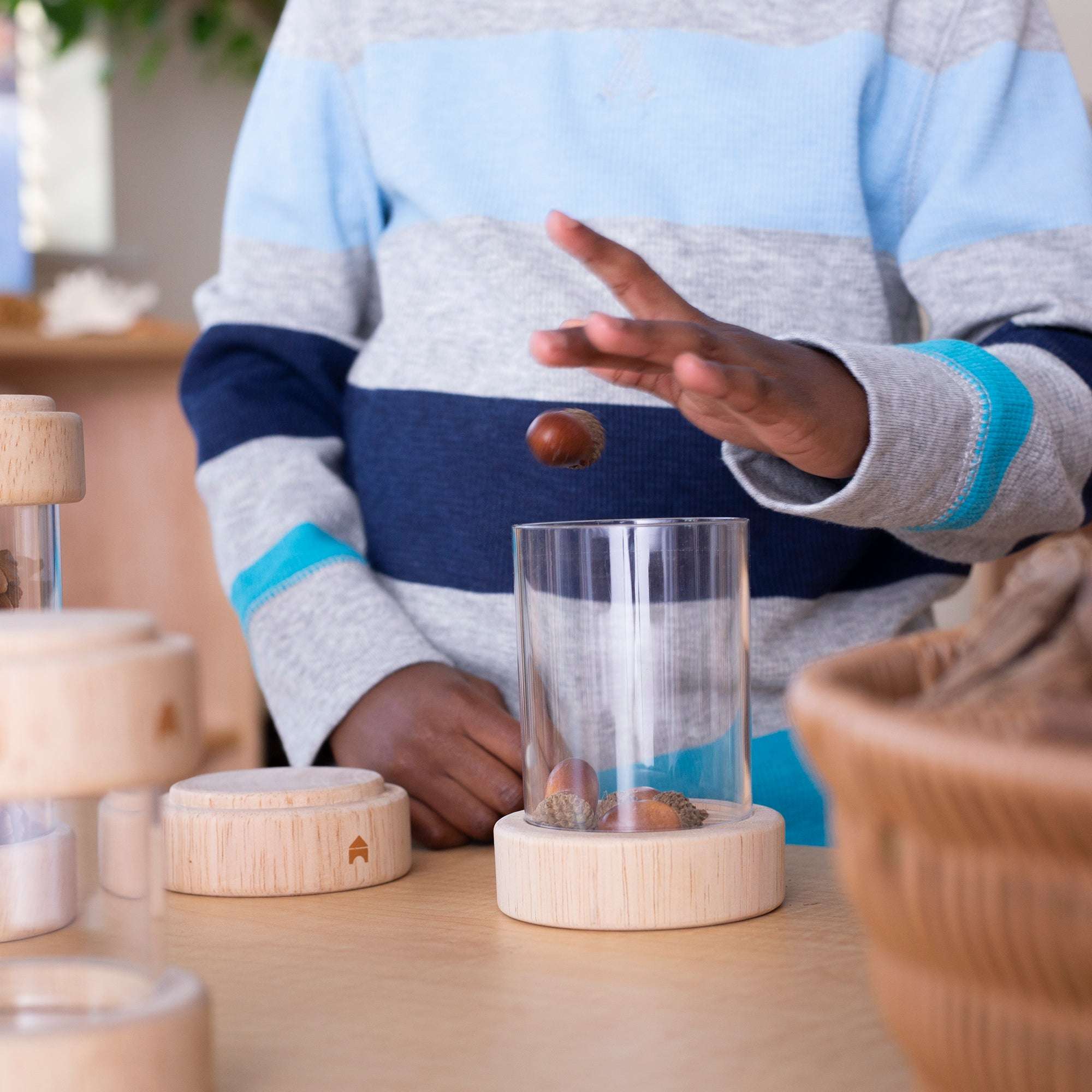Child placing an acorn into a clear, stackable acrylic Treasure Tube with a natural wooden base.