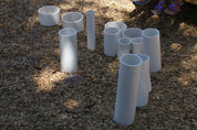 Assorted white rigid PVC tubes of varying lengths and diameters arranged on a wood chip surface for outdoor play.