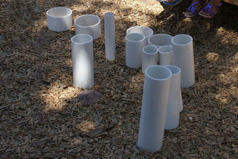 Assorted white rigid PVC tubes of varying lengths and diameters arranged on a wood chip surface for outdoor play.