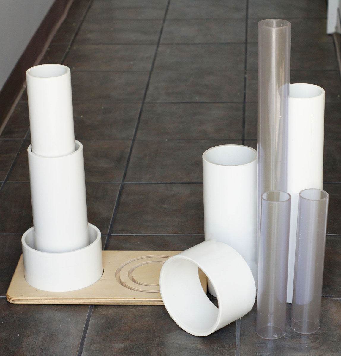 Set of white PVC and clear acrylic tubes of varying lengths with a flat wooden storage base for play.