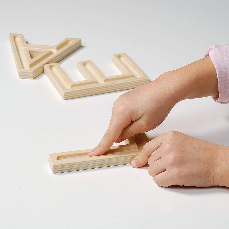 Child tracing a finger along the recessed groove of a light wood uppercase sensory letter block.