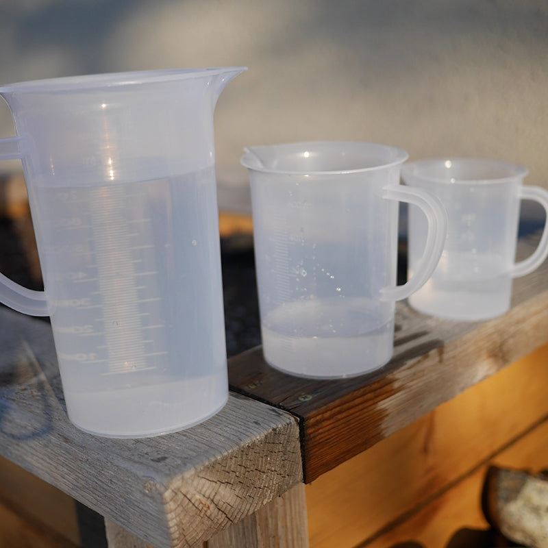 Three graduated, translucent polypropylene pitchers with handles and measurement markings on a wooden surface.