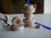 Stack of natural wooden wheels in various sizes with a blue plastic rod and a small canvas storage bag.
