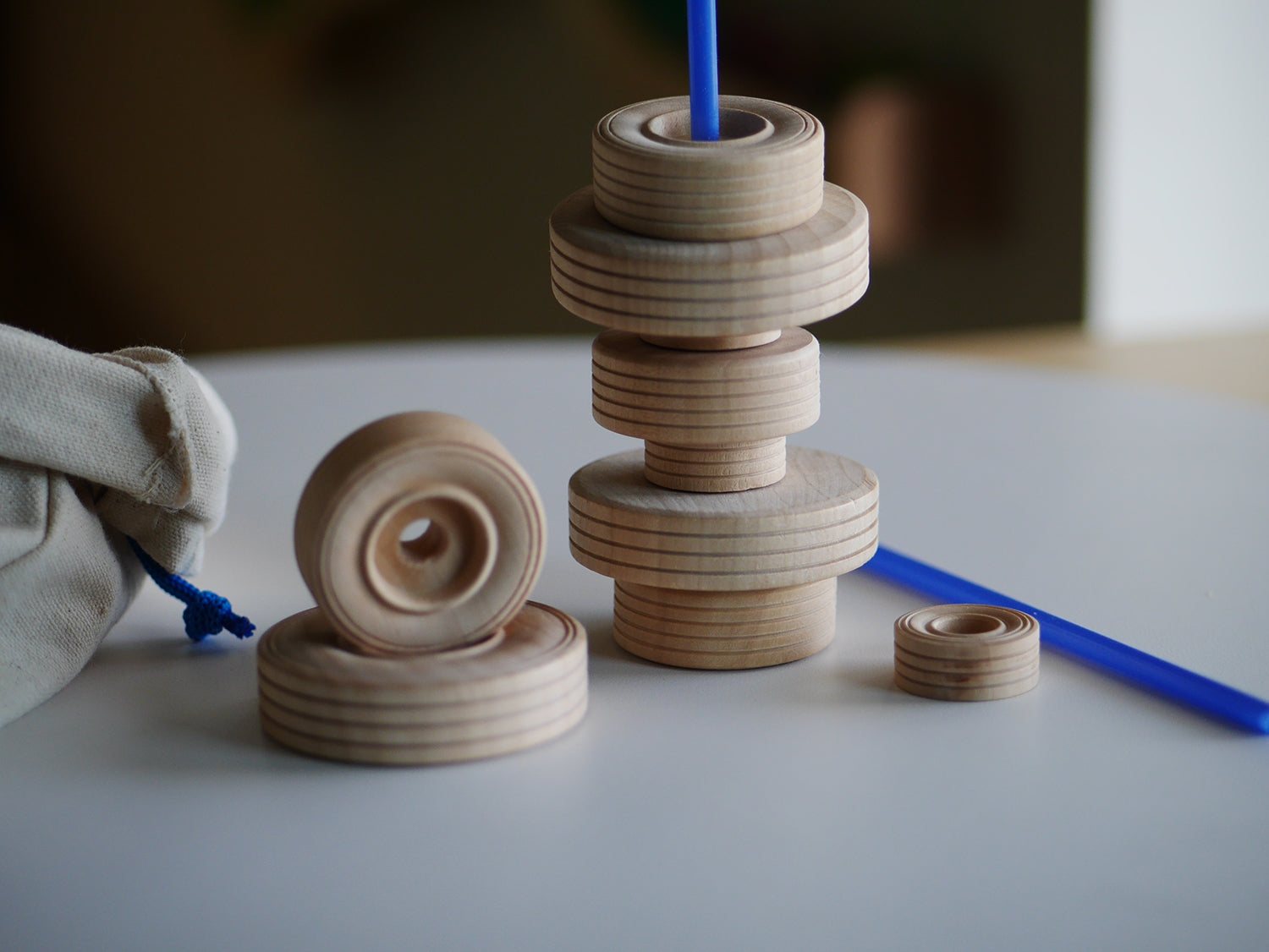 Stack of natural wooden wheels in various sizes with a blue plastic rod and a small canvas storage bag.