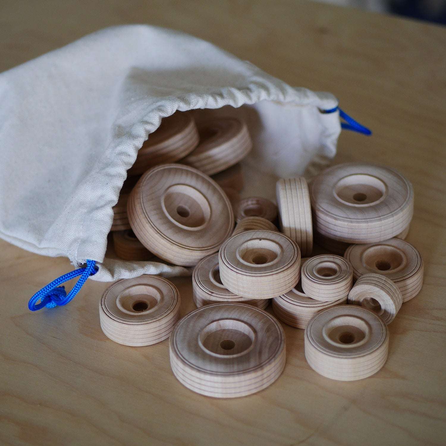 Set of natural wooden toy wheels in various sizes spilling from a white drawstring canvas storage bag.