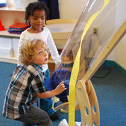 Children experimenting with a clear, pivoting wooden wind tunnel tube in a classroom setting.