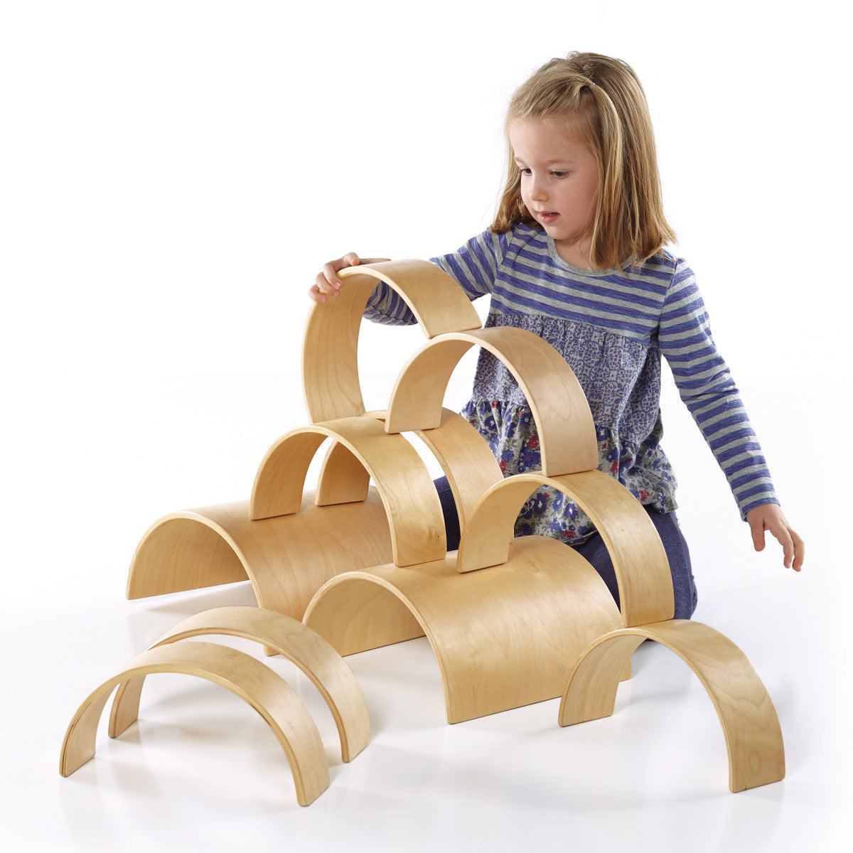 Young girl building with a set of natural birch wooden arches on a white background.