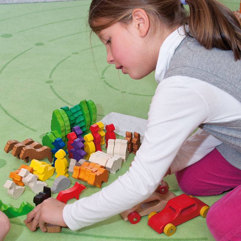 Child playing with colorful, minimalist hardwood farm animal figures and trees on a green rug.