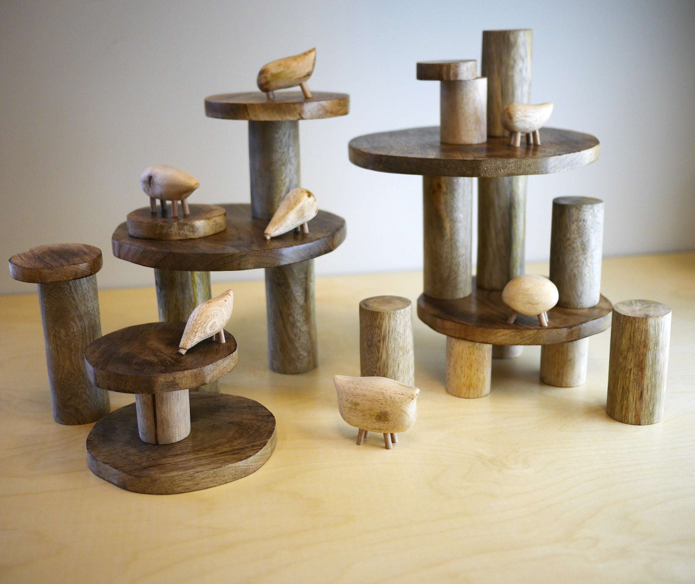 Natural wooden stacking discs and pillars arranged with small carved animal figures on a light wooden surface.