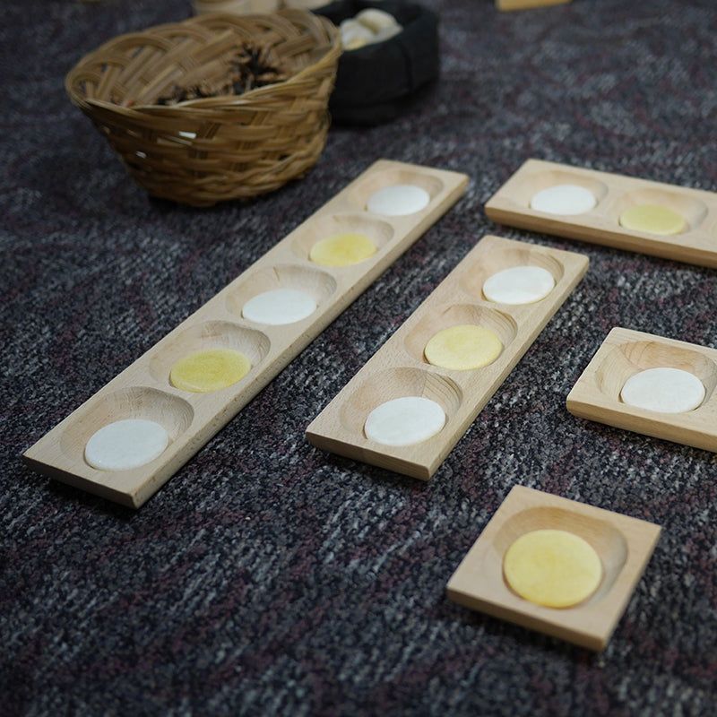 Set of five natural wooden sorting trays with circular indentations holding white and yellow discs on a grey carpet.