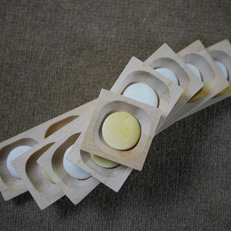 Five square wooden sorting trays with rounded indentations holding small yellow and white circular loose parts.