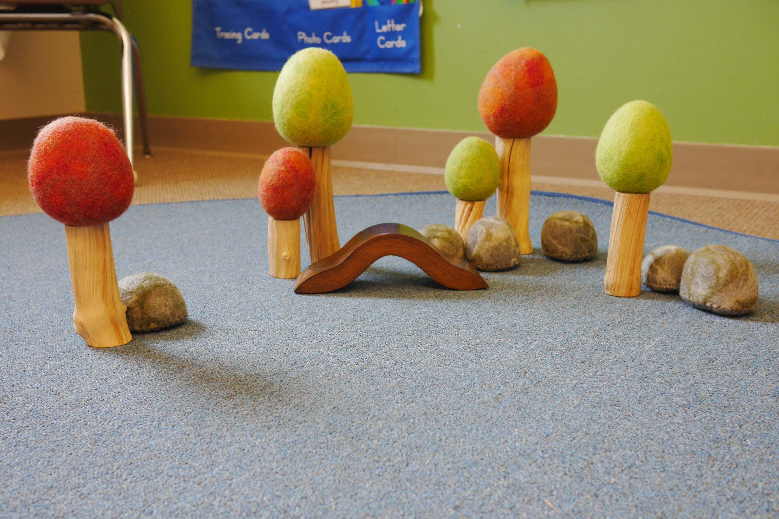 Artisanal wool trees with wooden trunks, a small wooden bridge, and felted river stones for imaginative play.