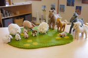Handmade felt wool farm animal figurines including sheep, horses, and pigs on a green felt play mat.