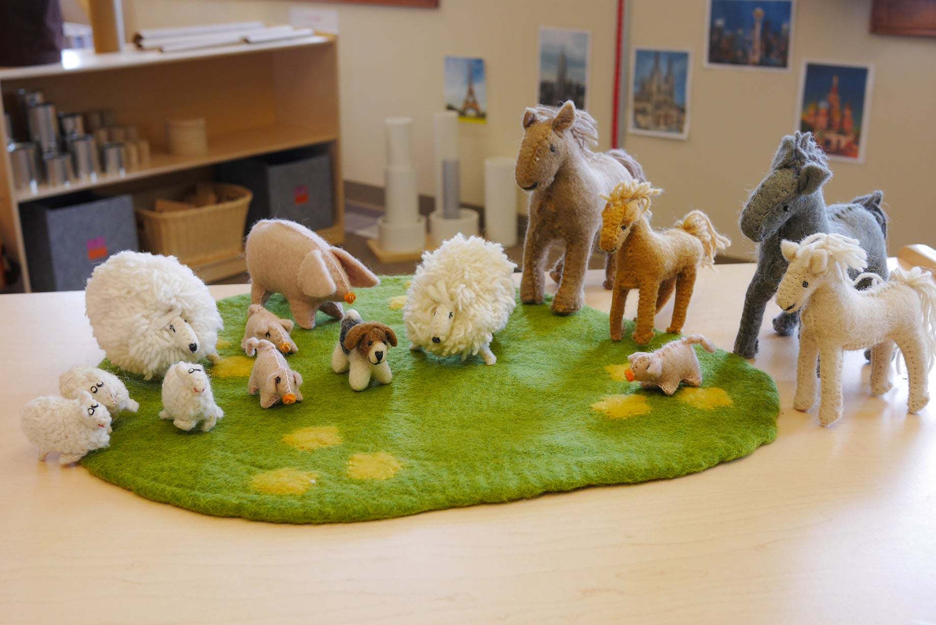 Handmade felt wool farm animal figurines including sheep, horses, and pigs on a green felt play mat.