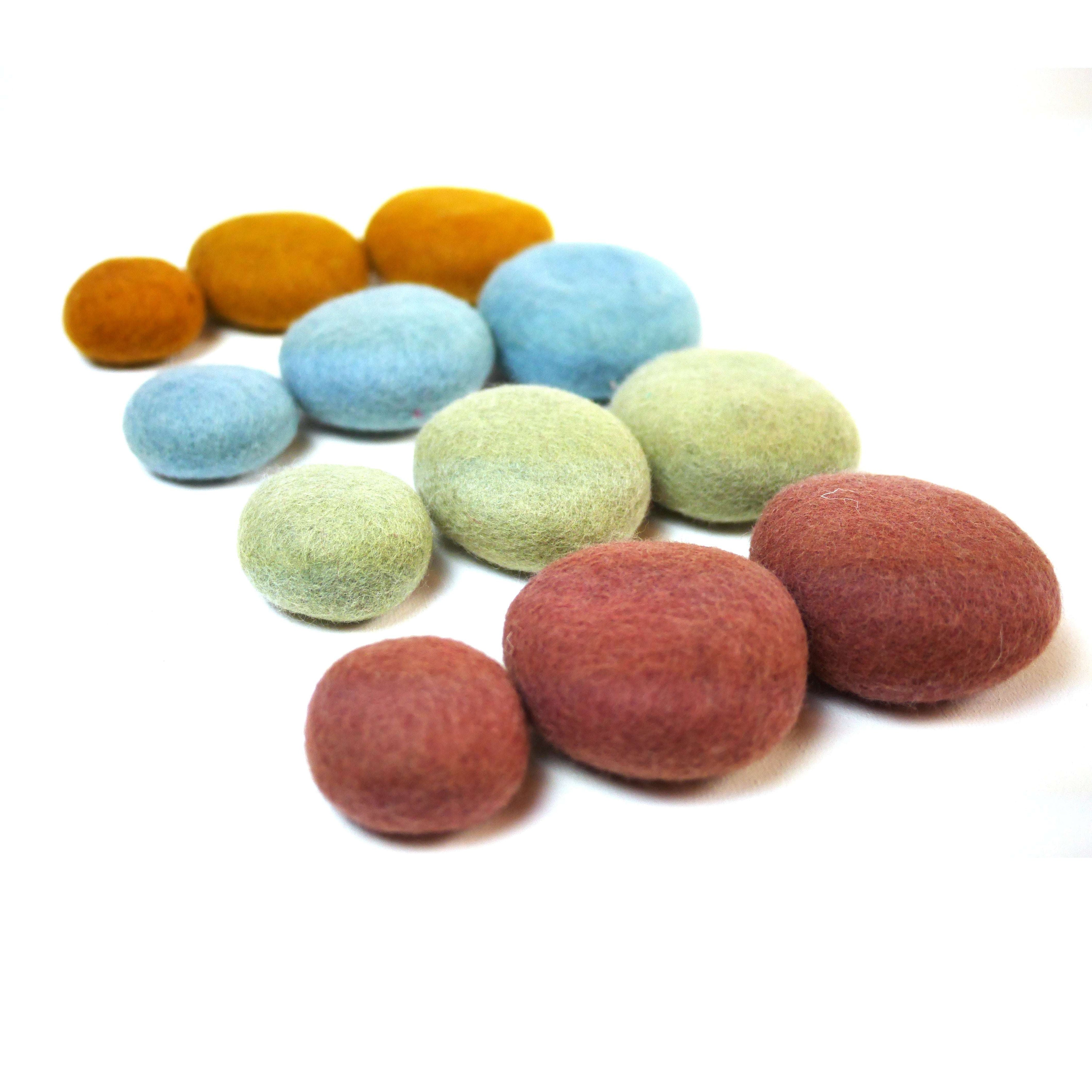 Twelve felted wool stacking pebbles in earth tones of sage, blue, brick, and gold arranged on a white background.